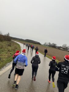 Nikolaus Community-Trailrun: Läufer mit Weihnachtsmützen auf regennasser Straße. - We Run 4 Fun!