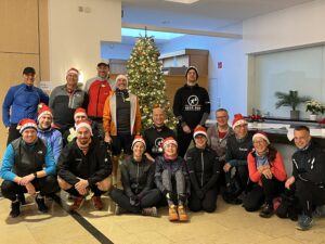 Gruppe von Läufern beim Nikolaus Community-Trailrun mit Weihnachtsmützen vor dem Weihnachtsbaum. "BEER RUN" Shirt. - We Run 4 Fun!