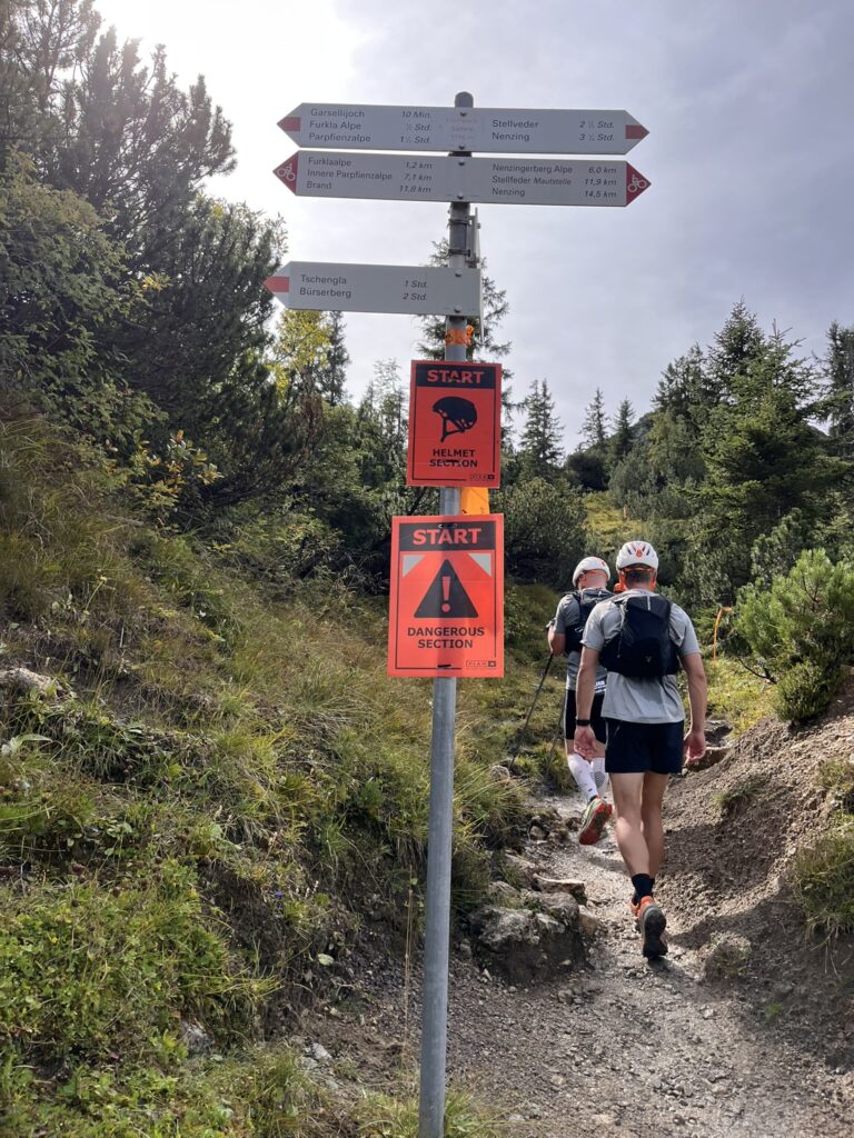 Wanderer auf dem Weg zum Transalpine Run 2025: Gefährlicher Abschnitt mit Helm-Pflicht. Wegweiser nach Furkla Alpe. - We Run 4 Fun!