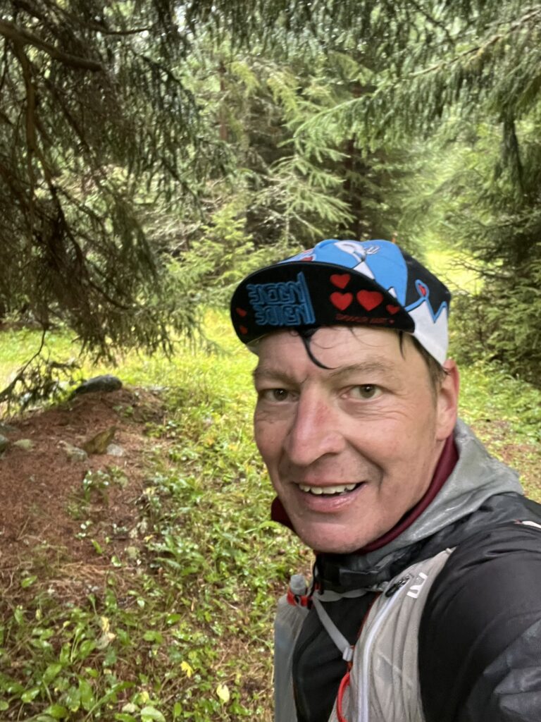 Läufer im Wald beim Transalpine Run 2025, mit Mütze und Rucksack. - We Run 4 Fun!