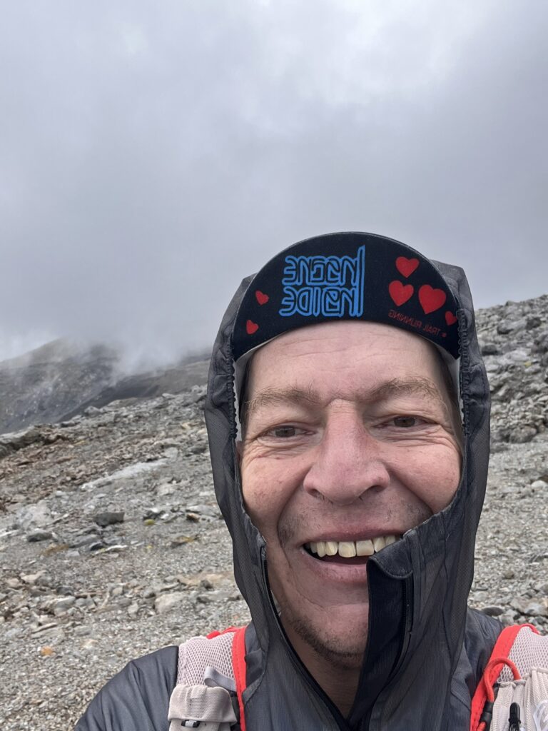 Lächelnder Mann beim Transalpine Run 2025, mit Regenjacke und Mütze. - We Run 4 Fun!