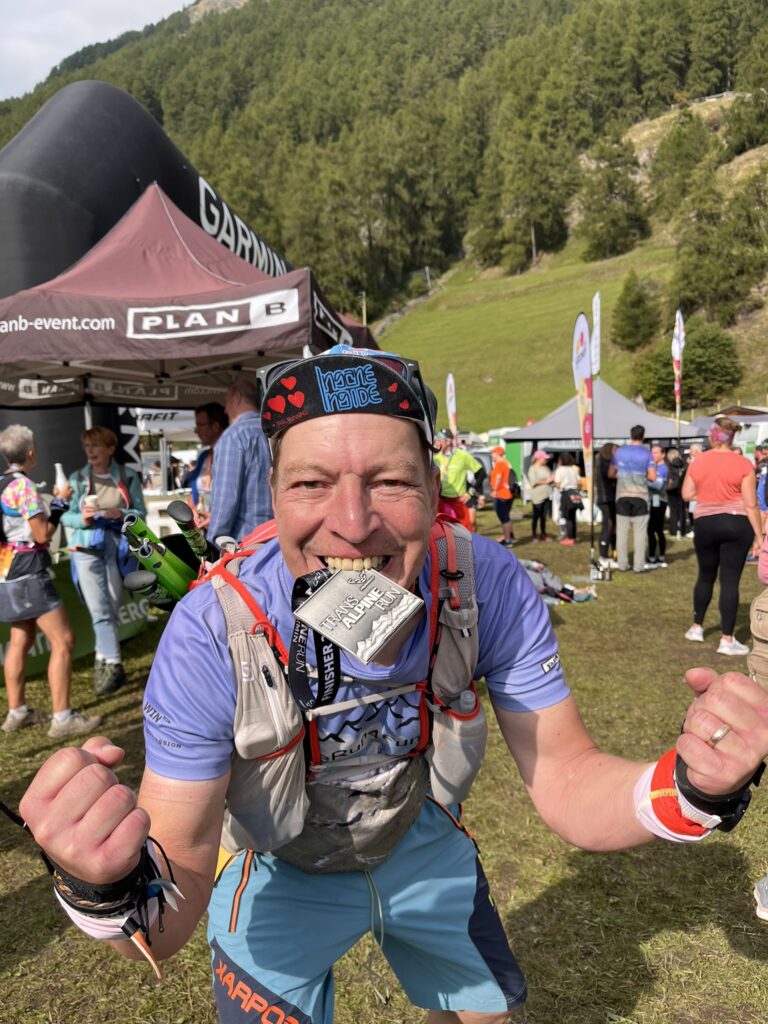 Glücklicher Finisher des Transalpine Run 2025 mit Medaille im Mund. Alpine Trail Running. - We Run 4 Fun!
